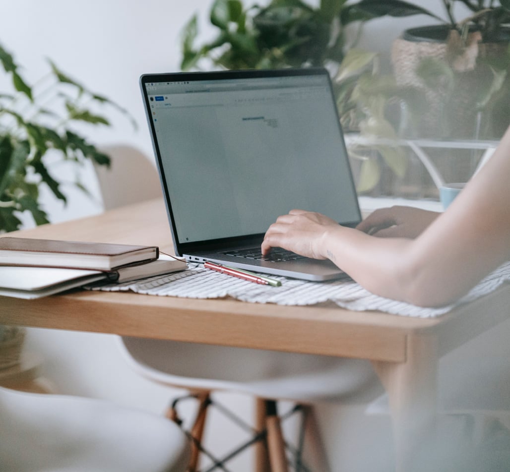 hands typing on a laptop beside plants